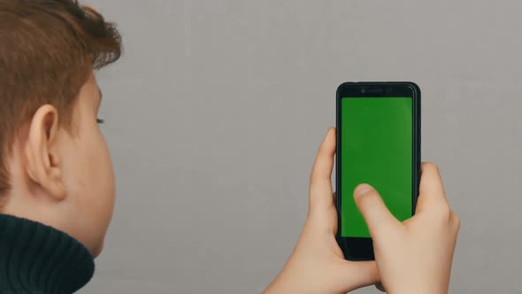 Teen Boy Holds in Hand a Black Smartphone with a Green Screen on White Background