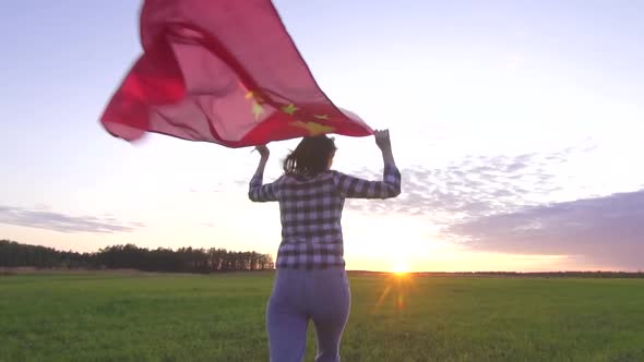 Young Positive Woman Runs Across the Field at Sunset with the Flag of China Slow Mo alt