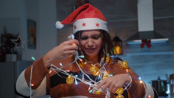 Festive Woman with Santa Hat Trying to Untangle Lights alt