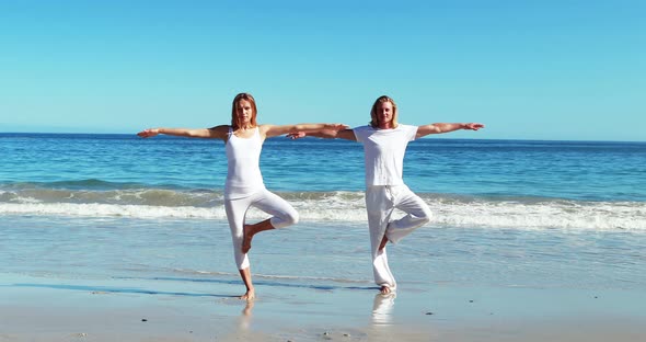 Couple performing yoga at beach alt