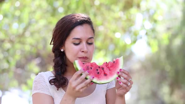 Beautiful young woman eating a slice of watermelon and smiling
