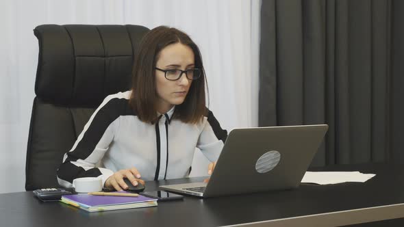 Woman works on laptop using computer mouse in modern office  alt
