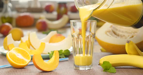 Melon Banana Orange Smoothie is Poured Into a Glass on the Background of Fresh Fruits alt