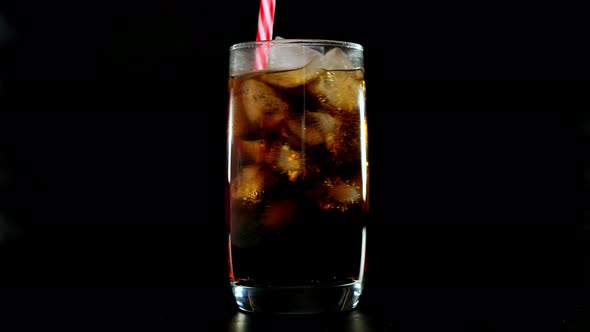 Putred Straw Into Cola with Ice Cubes in Glass Over Black Background. Close Up