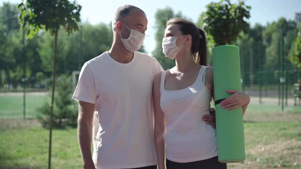 Positive Sportsman and Sportswoman in Covid-19 Face Masks Looking at Each Other and Talking alt