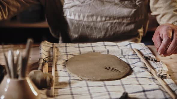 Young Woman Potter Makes a Design on the Clay Plate Using a Stamp in a Leaves Shape alt