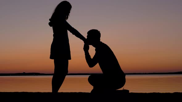 Man Sits On A Knee Then Takes The Woman Hand And Kisses Her At Sunset ...