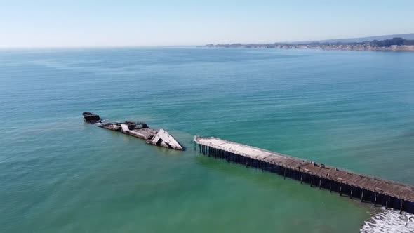 Concrete ship SS Palo Alto wreck near wooden pier, aerial rotate view. Sandy beach and endless ocean alt