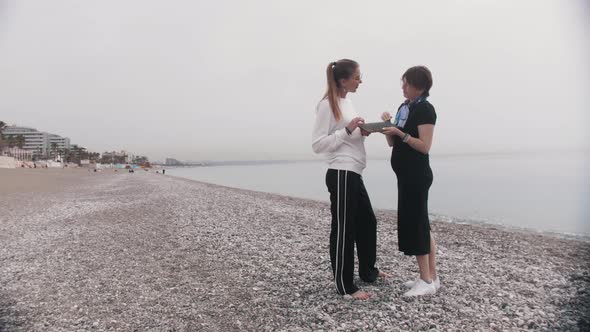 Two Women Standing on the Seashore  Talking and Touching the Sadhu Board alt