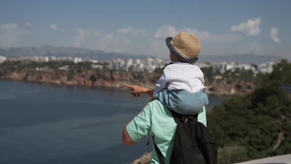 Mom Shows Toddler Sitting on Shoulders Views of Sea and Town alt
