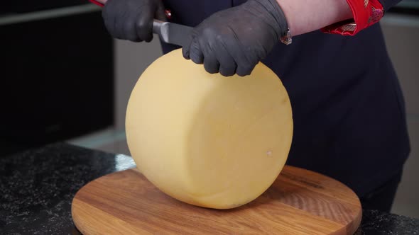 Women's Hands Cut a Round Piece of Hard Cheese with a Large Knife