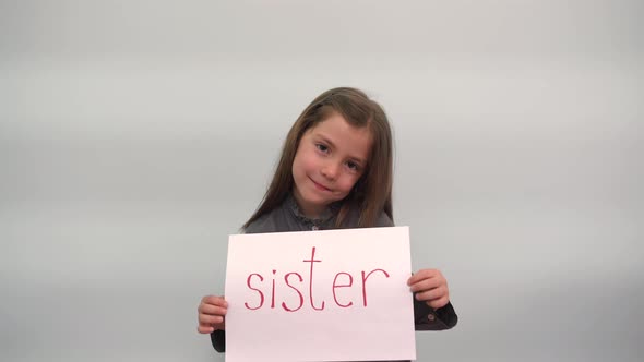 A Girl Holds a Piece of Paper with the Inscription SISTER and Smiles A Modest Child Shows a Sign