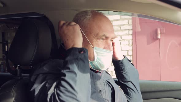 A Business Man at the Age of Sitting in a Car Puts on a Blue Medical Mask alt