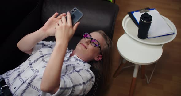 Attractive Businesswoman Having Video Call on Mobile Phone While Lying on Sofa at Office alt