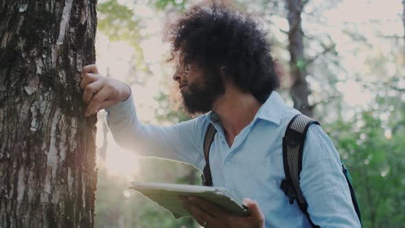 Male Curly Environmentalist Inspecting and Analyze Cover of Tree and Wood in Forest alt