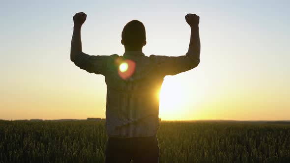 Silhouette of a Farmer Standing in a Field with Arms Raised alt