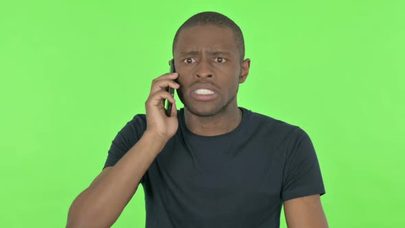 Angry Young African Man Talking on Phone on Green Background alt