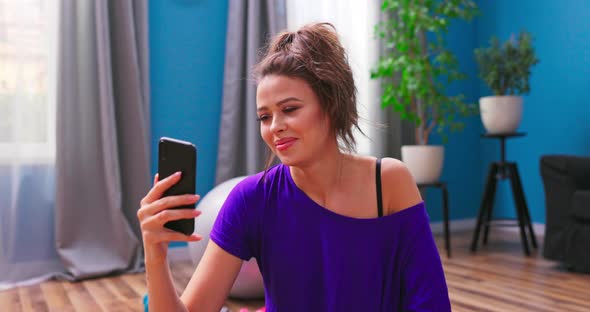 Pretty Young Woman Dressed in Fitness Clothes Chats on Video Chat with a Personal Trainer alt