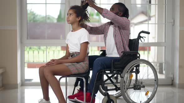 Concentrated Disabled African American Father Helping Daughter with Hairdo at Home Indoors alt