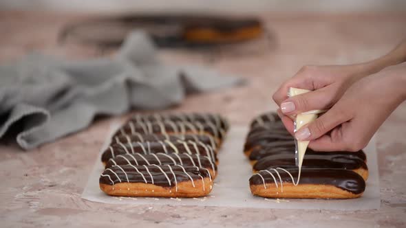 Pastry chef pours white chocolate on French eclairs.	