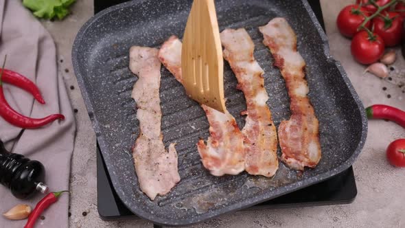 Cooking Pieces of Flavorful Sliced Organic Bacon Fried in Grill Pan alt