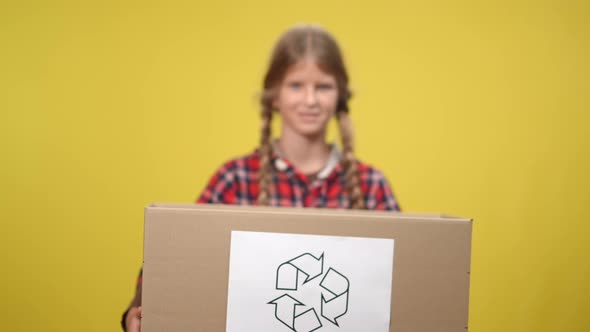 Closeup Box with Recycle Symbol and Blurred Teenage Girl at Yellow Background alt