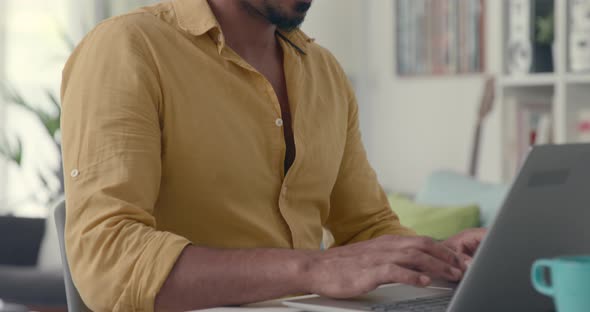 Young man sitting at desk and working with his laptop at home, remote work concept