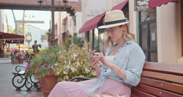  Slow Motion Europe Vacation. Pretty Woman Is Checking Phone Relaxing on Bench alt