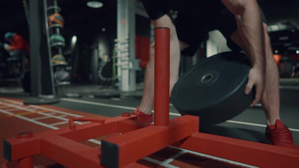 Man Putting Barbell Plate on Gym Stand alt