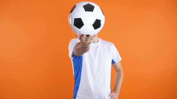 Football Fan In White Blue Shirt Standing Still and Holding Ball in Front of His Face with One Hand alt