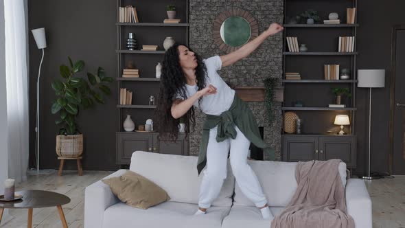Young Attractive Fun Cute Joyful Woman Jumping on Sofa in Living Room Funny Dancing Actively alt