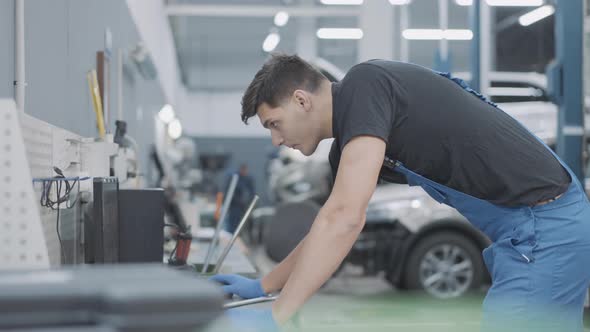 Side View Portrait of Concentrated Caucasian Service Man in Uniform Standing in Auto Repair Shop alt