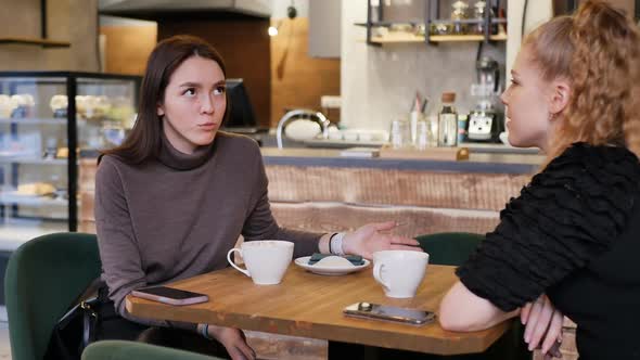 Young Blonde and Brunette at a Table in a Restaurant Talking and Drinking Tea alt
