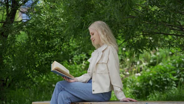 Romantic Young Woman Reads a Book Relaxed in the Park Among the Trees