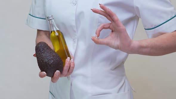 Nutritionist Doctor Holding Organic Avocado Fruit and Bottle of Oil alt