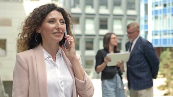 Portrait of a Middleaged Businesswoman Talking on a Mobile Phone in the Courtyard of a Large alt