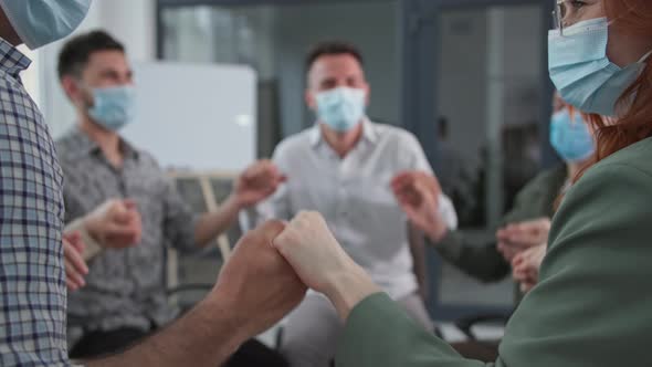 Male and Female Work Team Wearing Medical Masks Raise and Lower Their Arms While Sitting in a Circle
