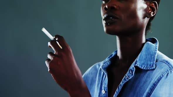 Androgynous man posing with cigarette against dark background alt