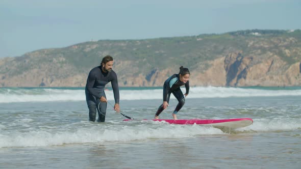 Long Shot of Happy Girl Standing on Surfboard with Help of Coach alt