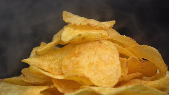 Craft crispy hot potato chips with smoke rotating on black background close up. Golden fried alt