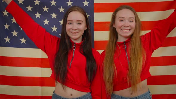 Happy Young Twin Sisters Posing with US Flag Wrapping in National Symbol Hugging Smiling Looking at alt