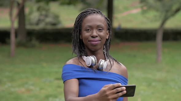 Pretty young black african woman taking selfie and smiling at camera in the park alt