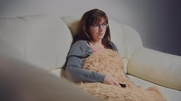 Happy Woman with Glasses Sitting on the Sofa in the Evening and Watching Tv Switches Channels