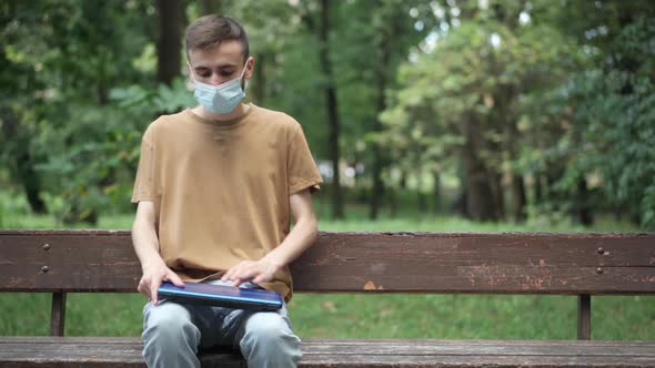 Confident Young Caucasian Man Sitting on Bench in Summer Park and Opening Laptop alt