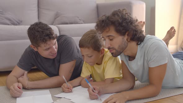 Focused Relaxed Fathers and Son Lying on Floor and Drawing alt