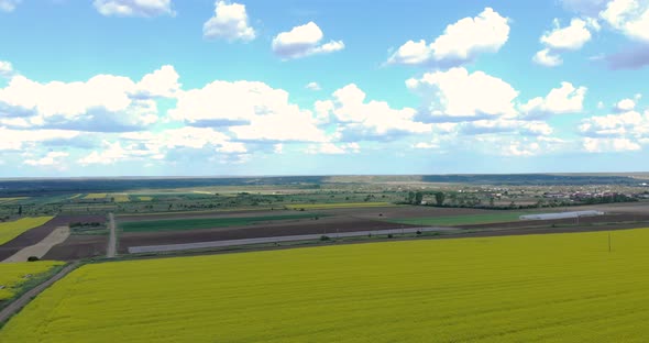 Picturesque View Of A Countryside With Village And Canola Farmland Against Blue Cloudy Sky. - Aerial alt