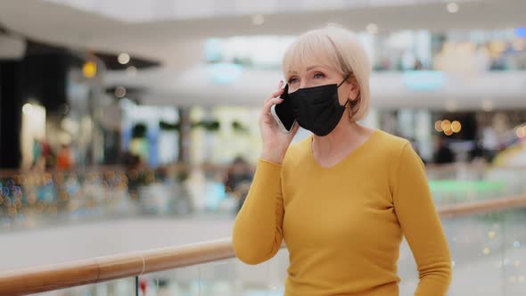 Caucasian Middleaged Woman in Medical Protective Mask Walking in Mall Speaking on Telephone alt