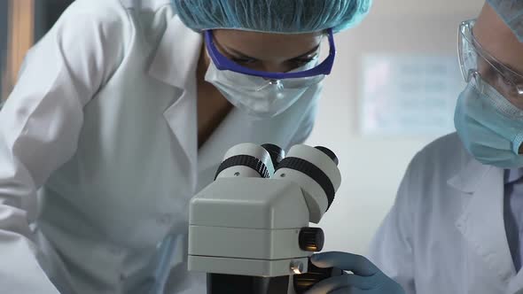 Scientist and Lab Assistant Looking Into Microscope at Reaction of Samples alt