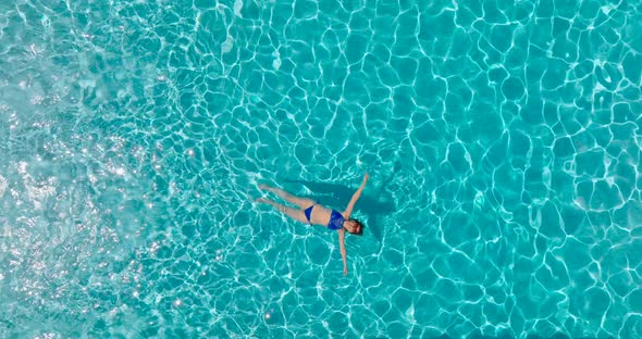 Top Down View of a Woman in a Blue Swimsuit Lying on Her Back in the Pool alt