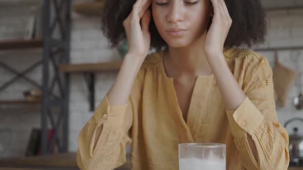Afro-American Girl Sits at the Table with a Headache. She Sits and Touches Her Temples. She Has Her alt